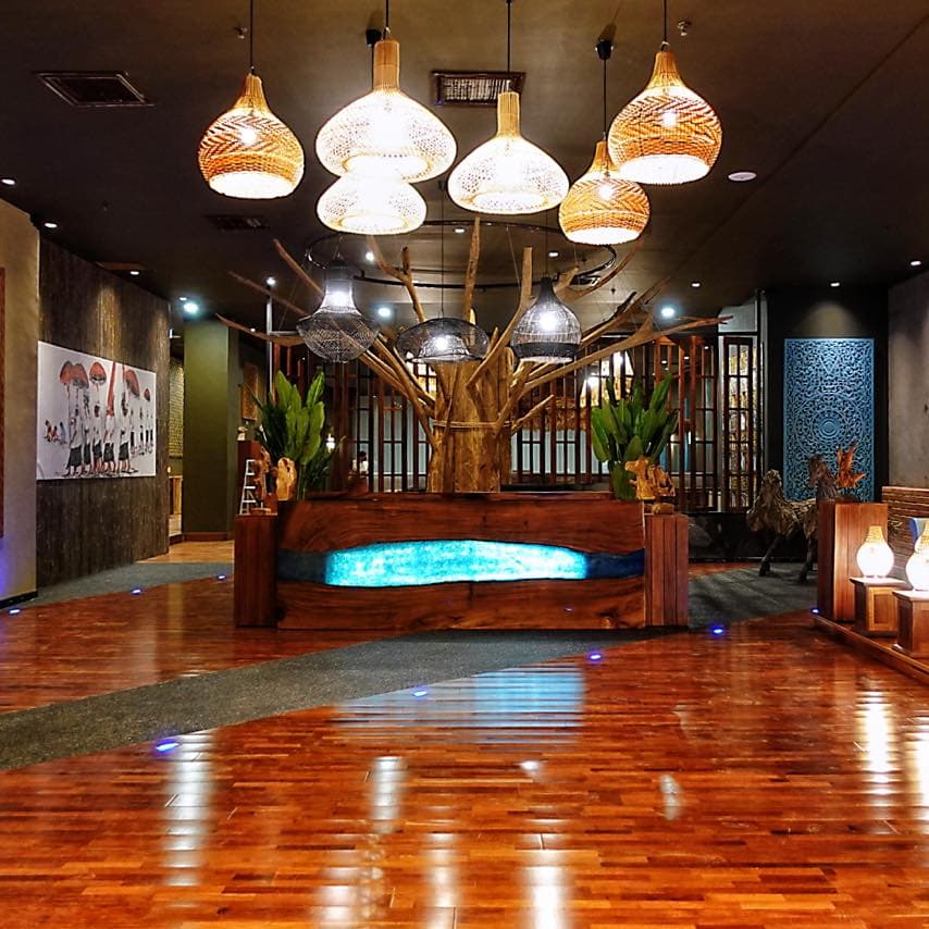 Modern lobby featuring a blue-lit wooden desk, woven pendant lights, and decorative tree sculpture.