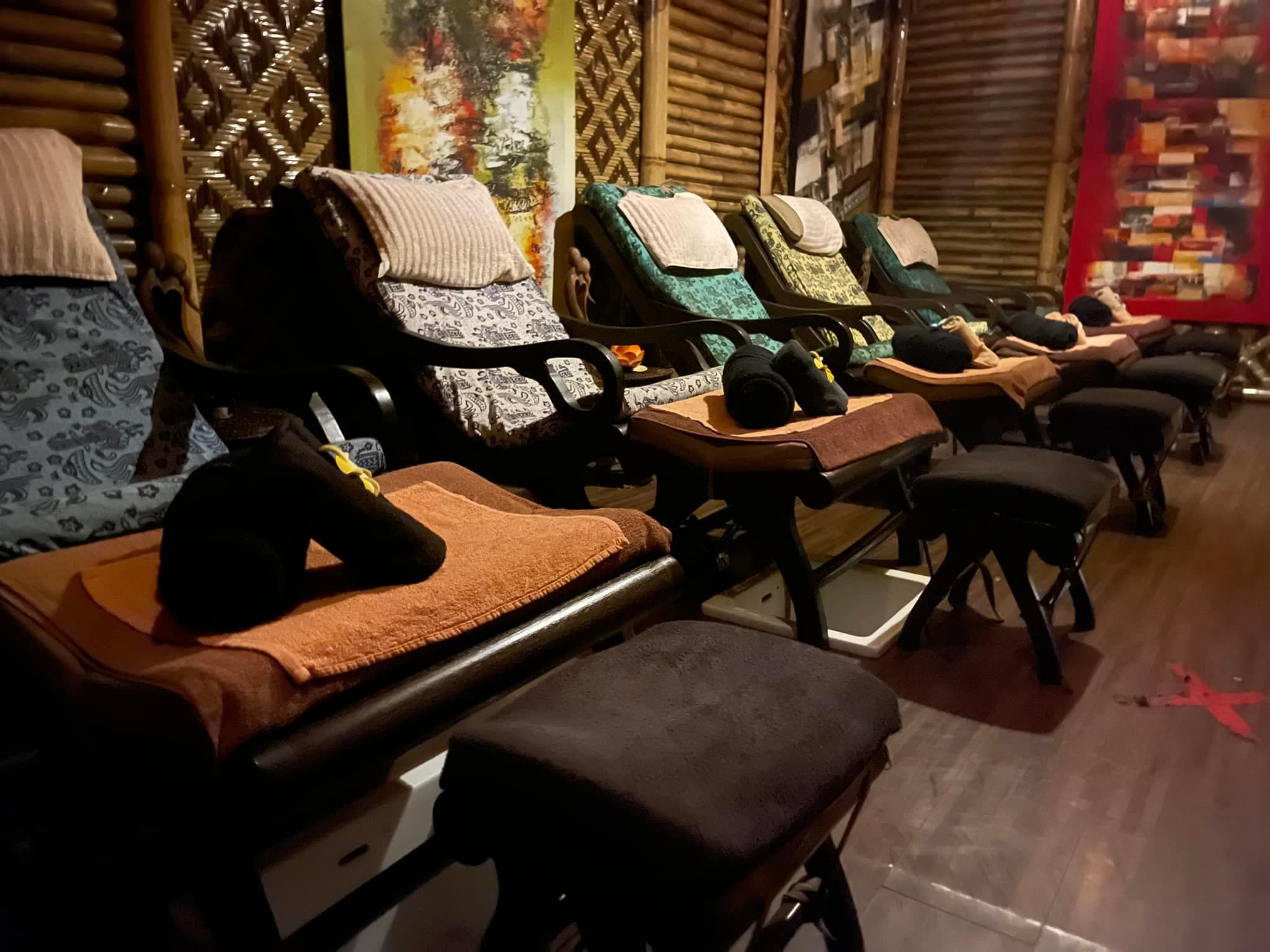 Row of reclining spa chairs with patterned cushions and footstools in a cozy bamboo-walled room.