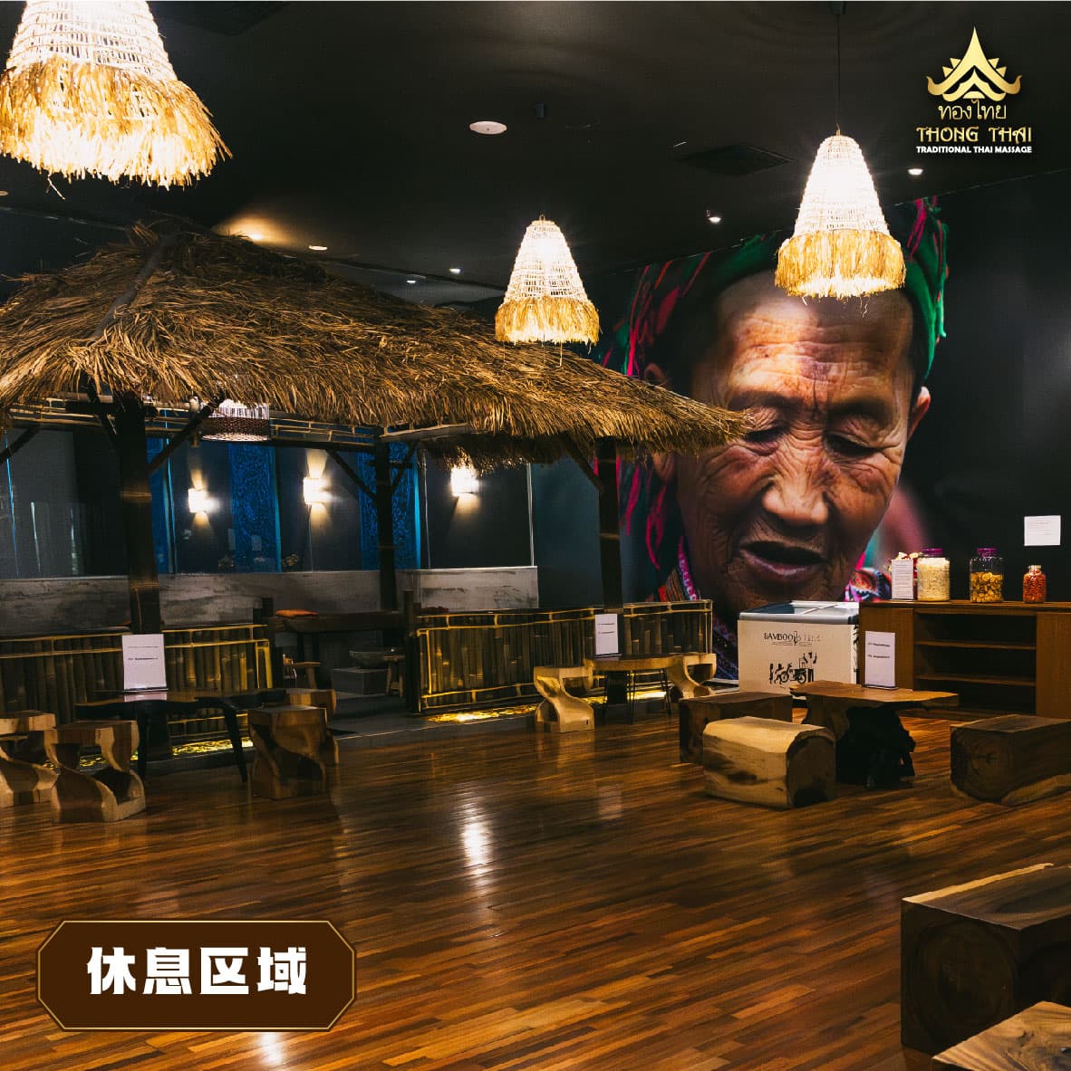 Thai massage rest area with thatched hut, wooden log seating, and large wall mural.